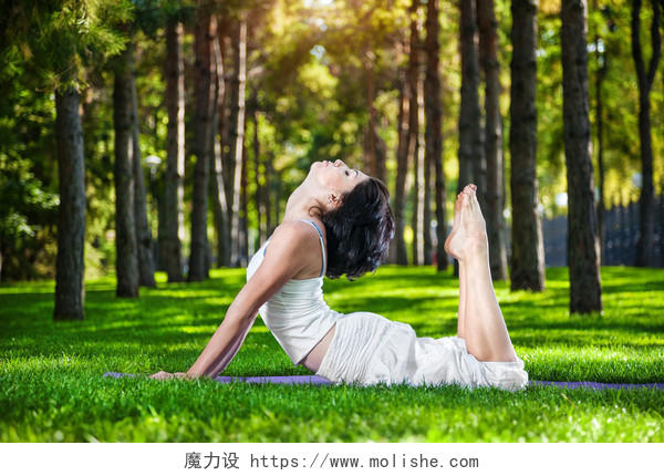 在做瑜伽 在公园里绕着松树的绿色草地上的白色衣服的女人产后瑜伽户外瑜伽